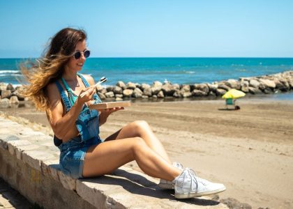 Woman in casual attire eating sushi outdoors on a sunny beach day.